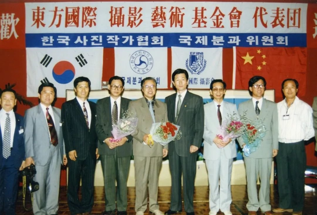 1993年8月，基金会代表团访问韩国受到热烈欢迎，基金会副主席冯德英、秘书长曾毅及代表团成员夏立汉在欢迎仪式上与韩国写真作家协会成员留影。